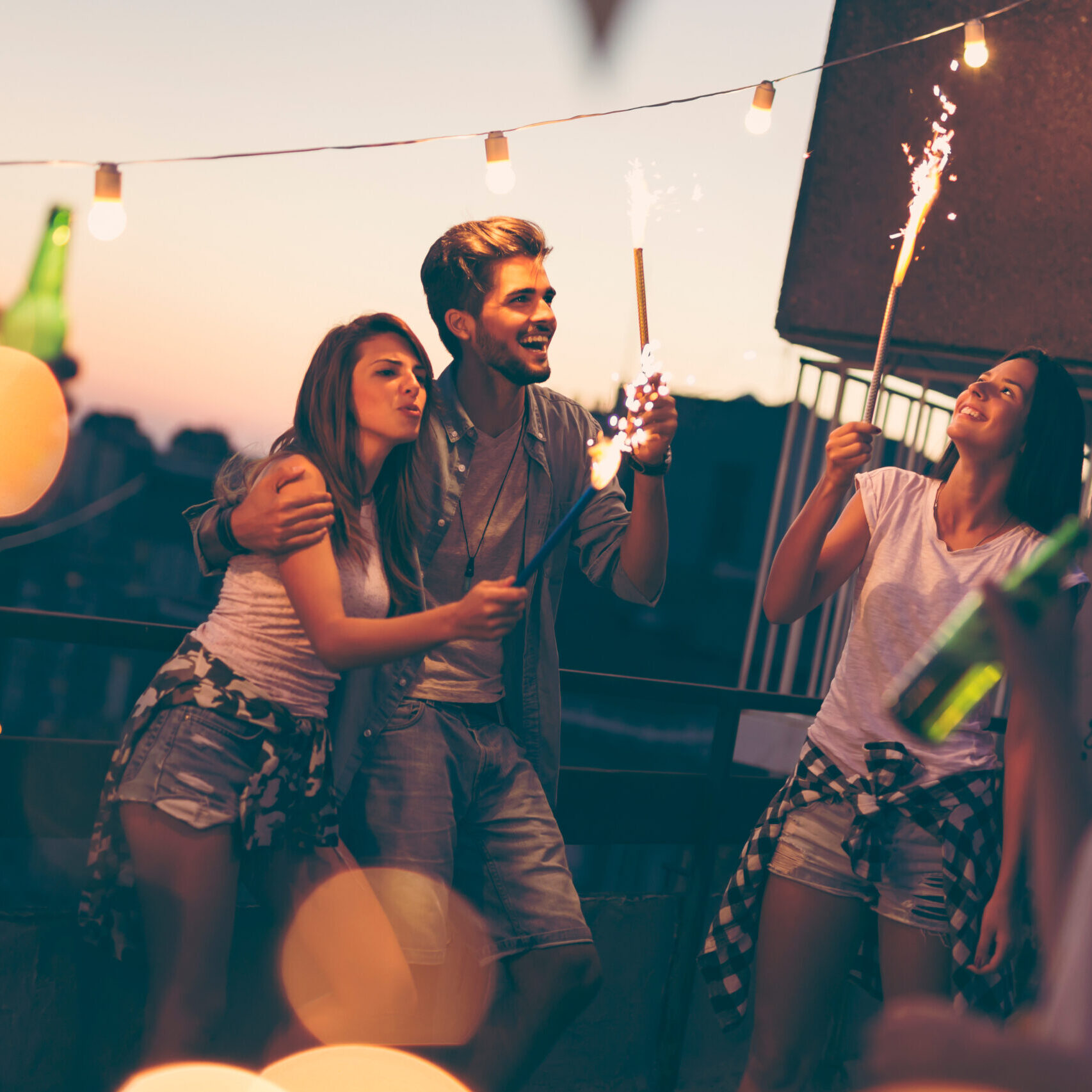 Group of young friends having fun at a rooftop party, singing, dancing and waving with sparklers