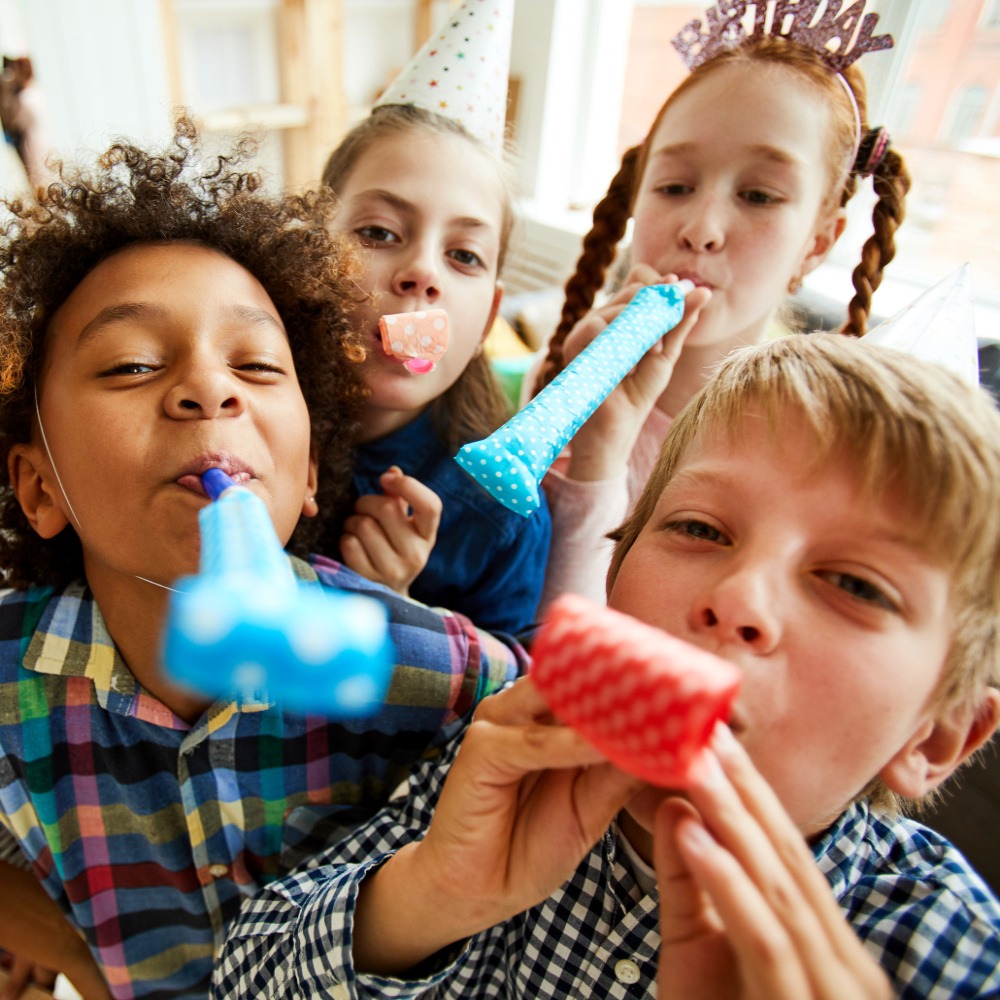 High angle view at multi ethnic group of children blowing party horns at camera